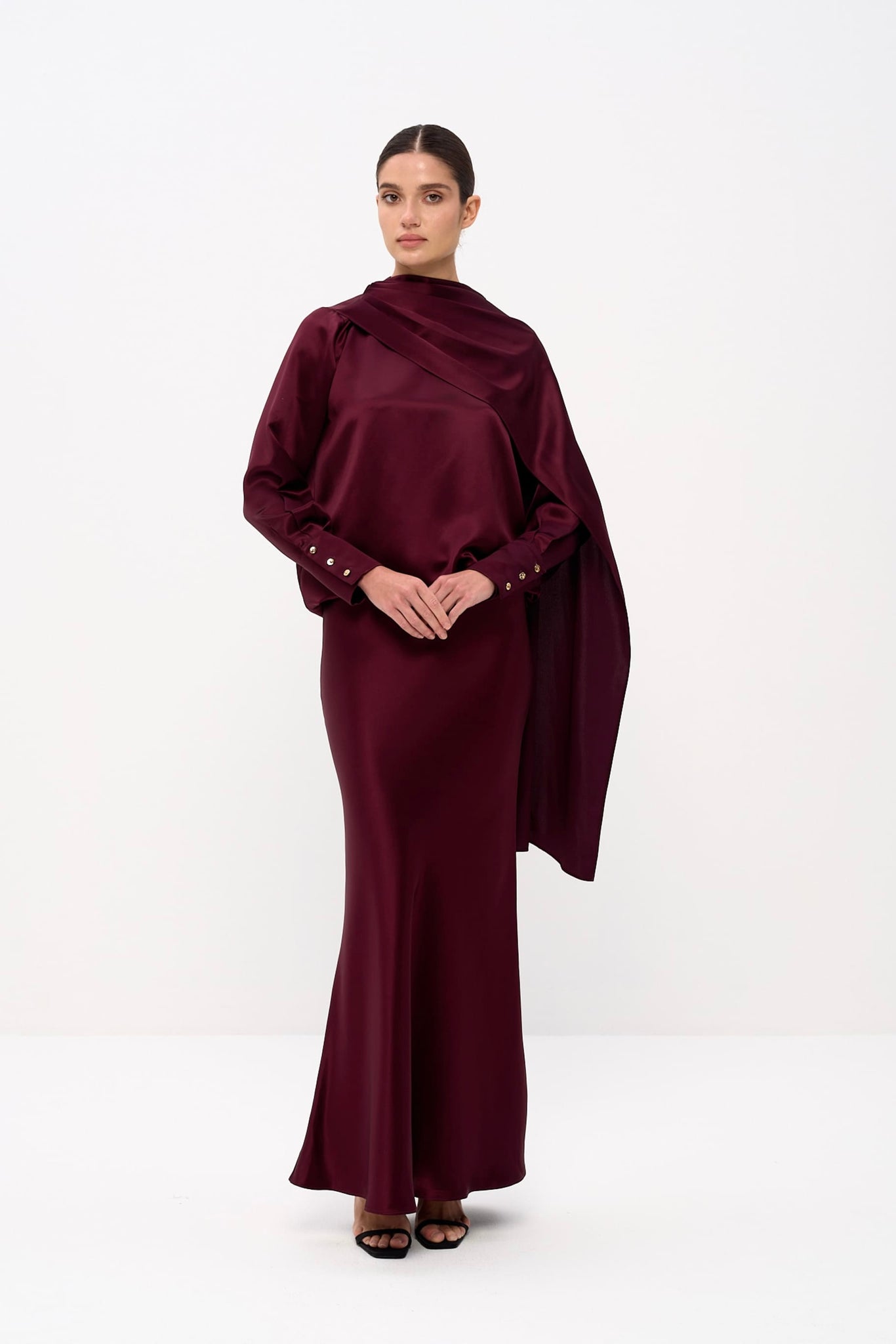 Woman wearing a burgundy dress with a draped fabric on a white background