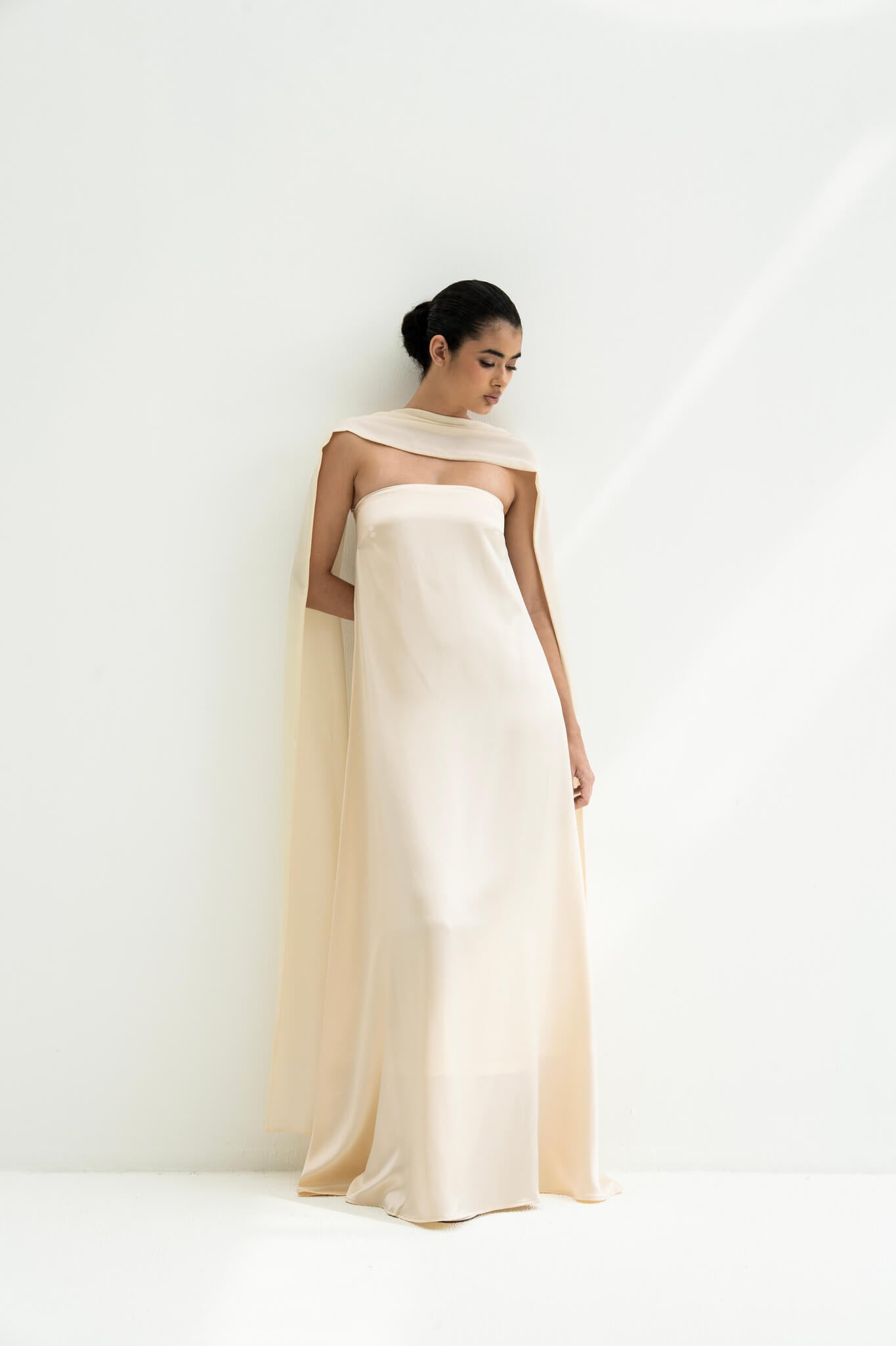 Woman wearing a strapless white gown with a long scarf on a white background