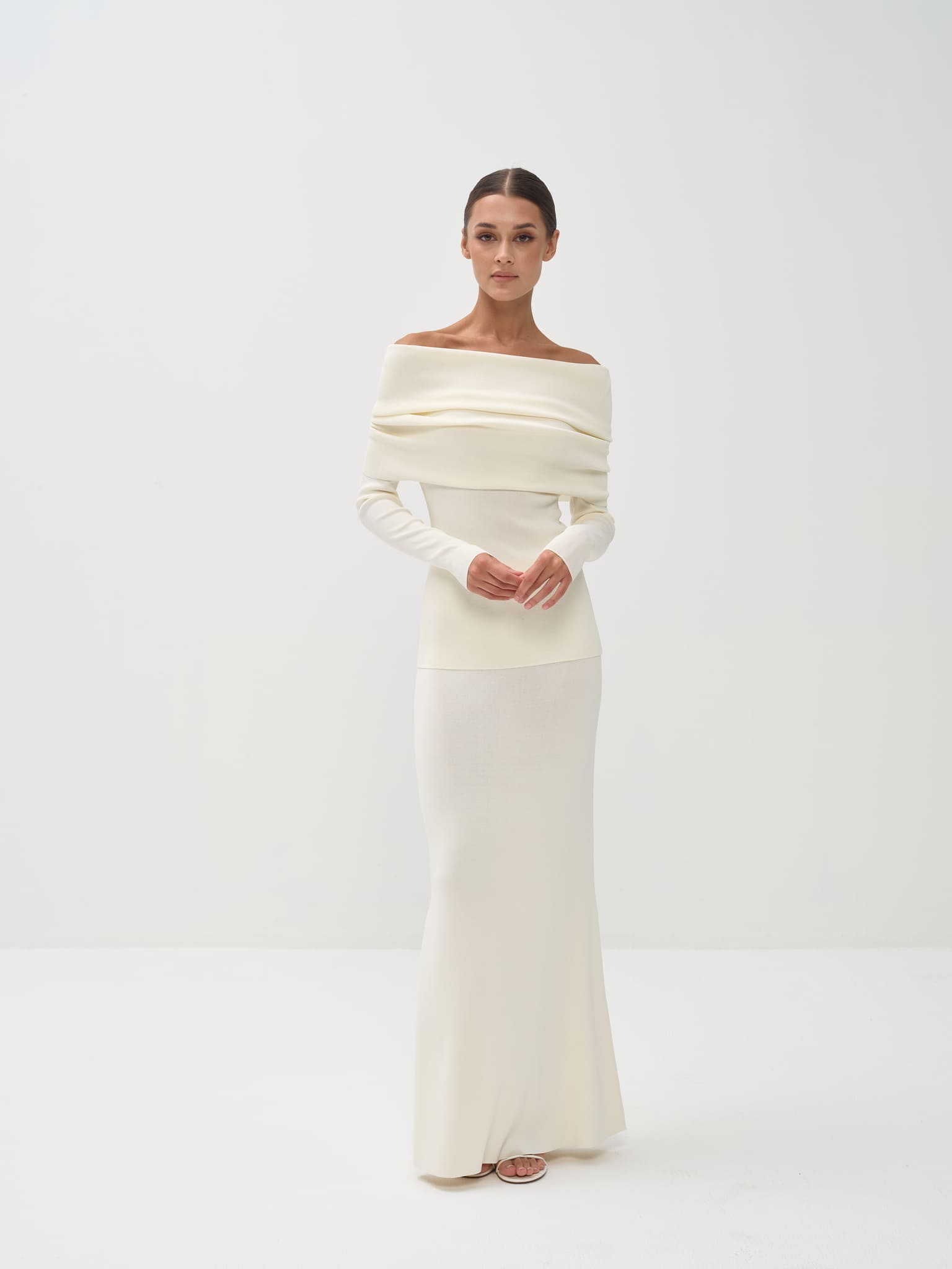 Woman wearing a white off-shoulder gown against a plain background