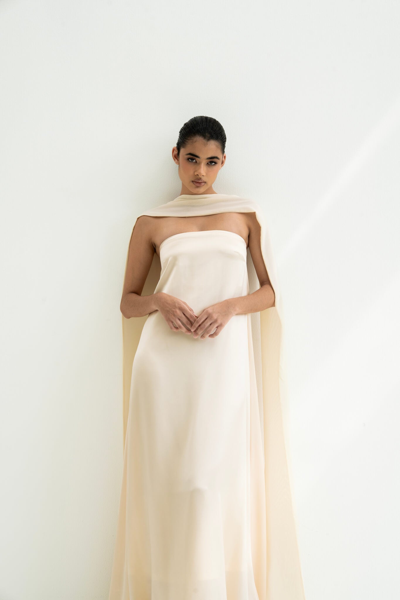 Woman wearing a strapless white gown with a long scarf on a white background