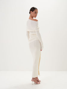 A model wearing a white asymmetric draped neckline top and a matching long skirt, with accessories and shoes.