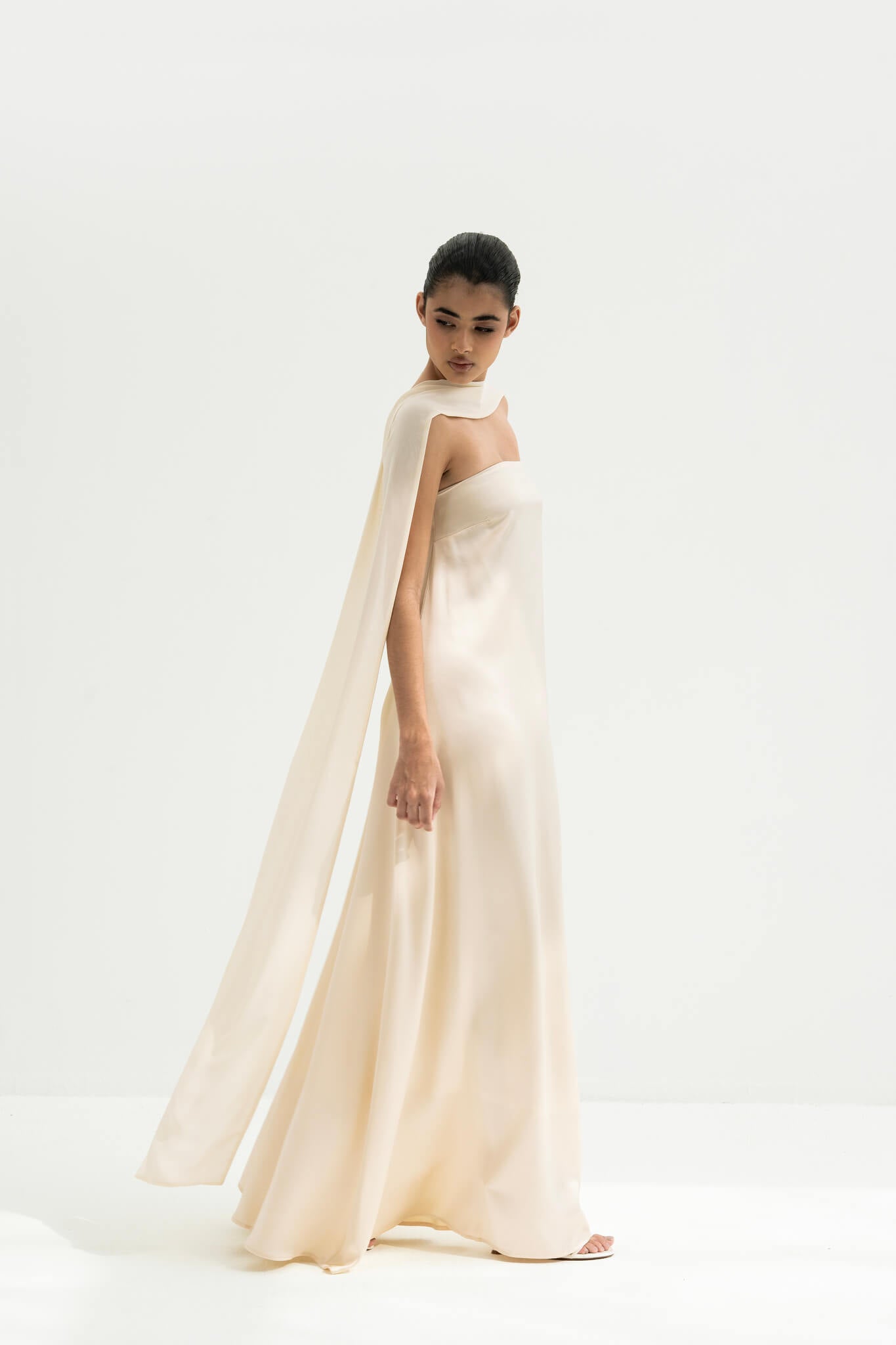 Woman wearing a strapless white gown with a long scarf on a white background