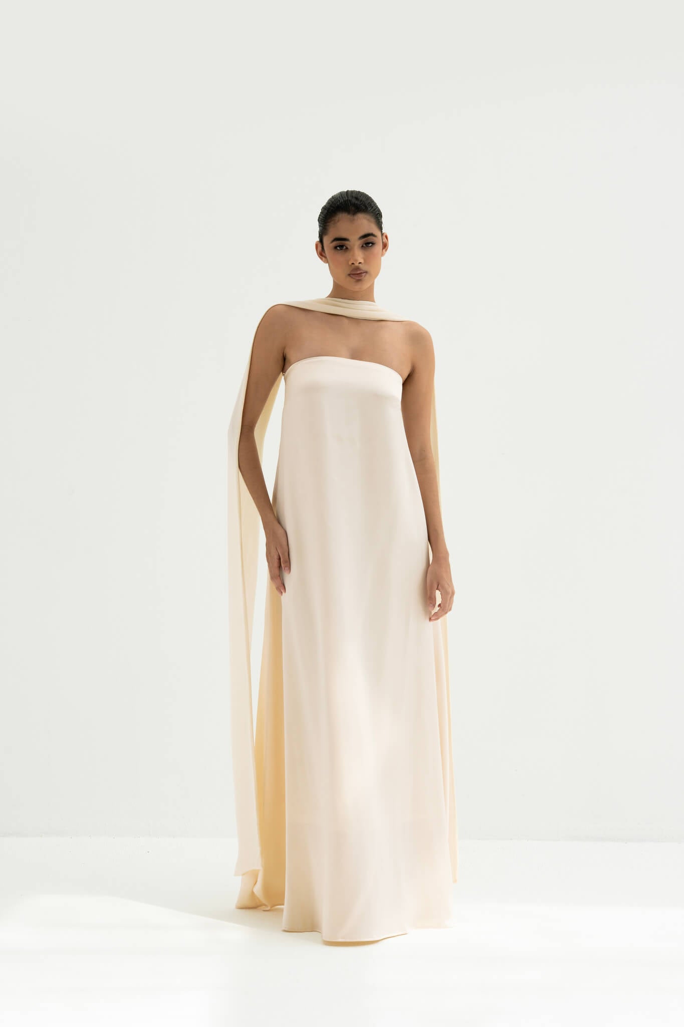 Woman wearing a strapless white gown with a long scarf on a white background