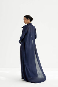 Woman wearing a long, dark blue dress with sheer overlay on a white background