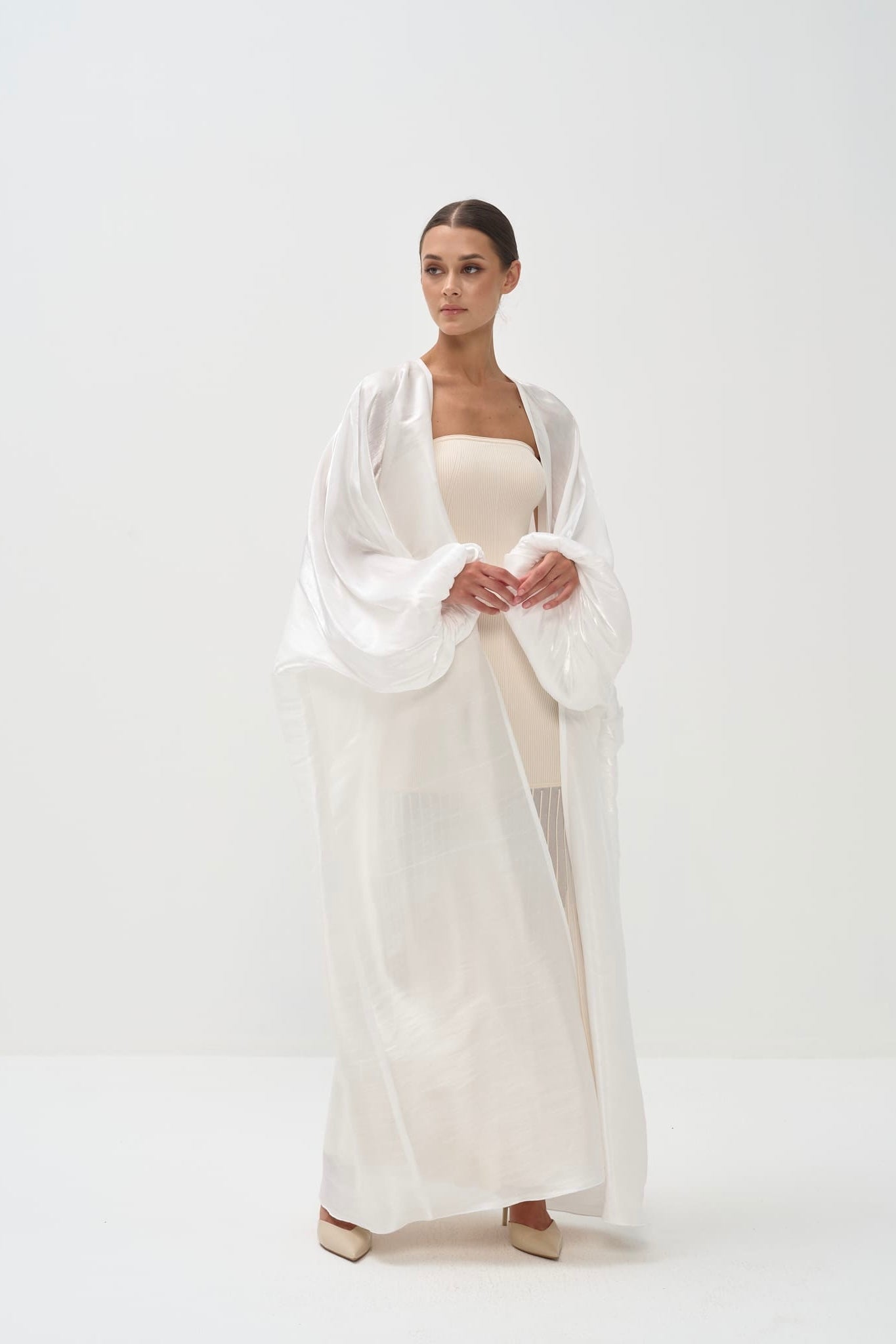 Woman wearing a white dress with a sheer white shawl on a white background