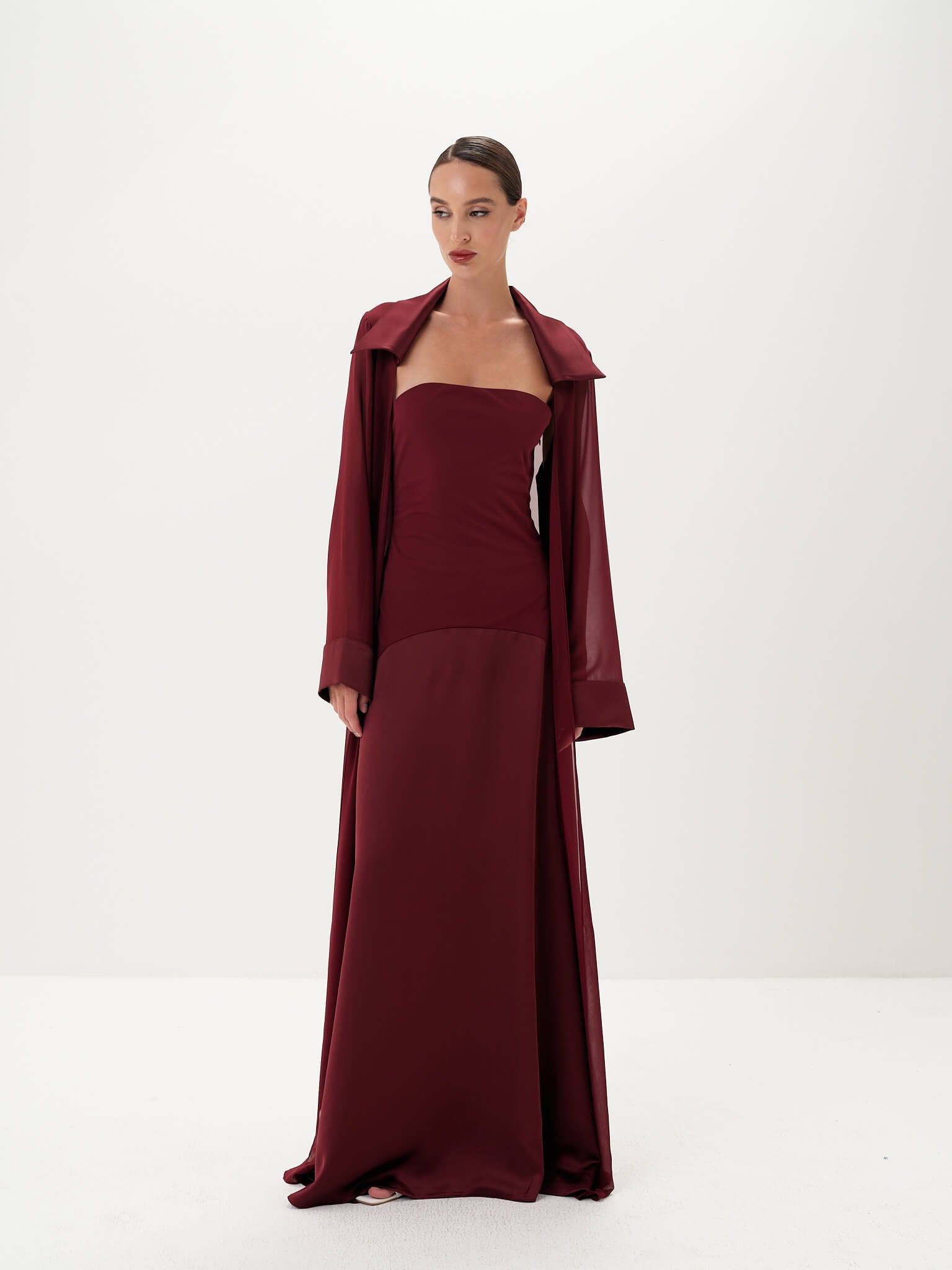 Woman wearing a burgundy dress with matching coat on a white background
