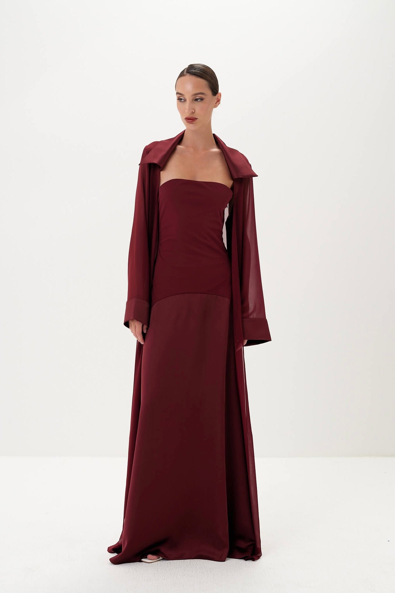 Woman wearing a burgundy dress with matching coat on a white background