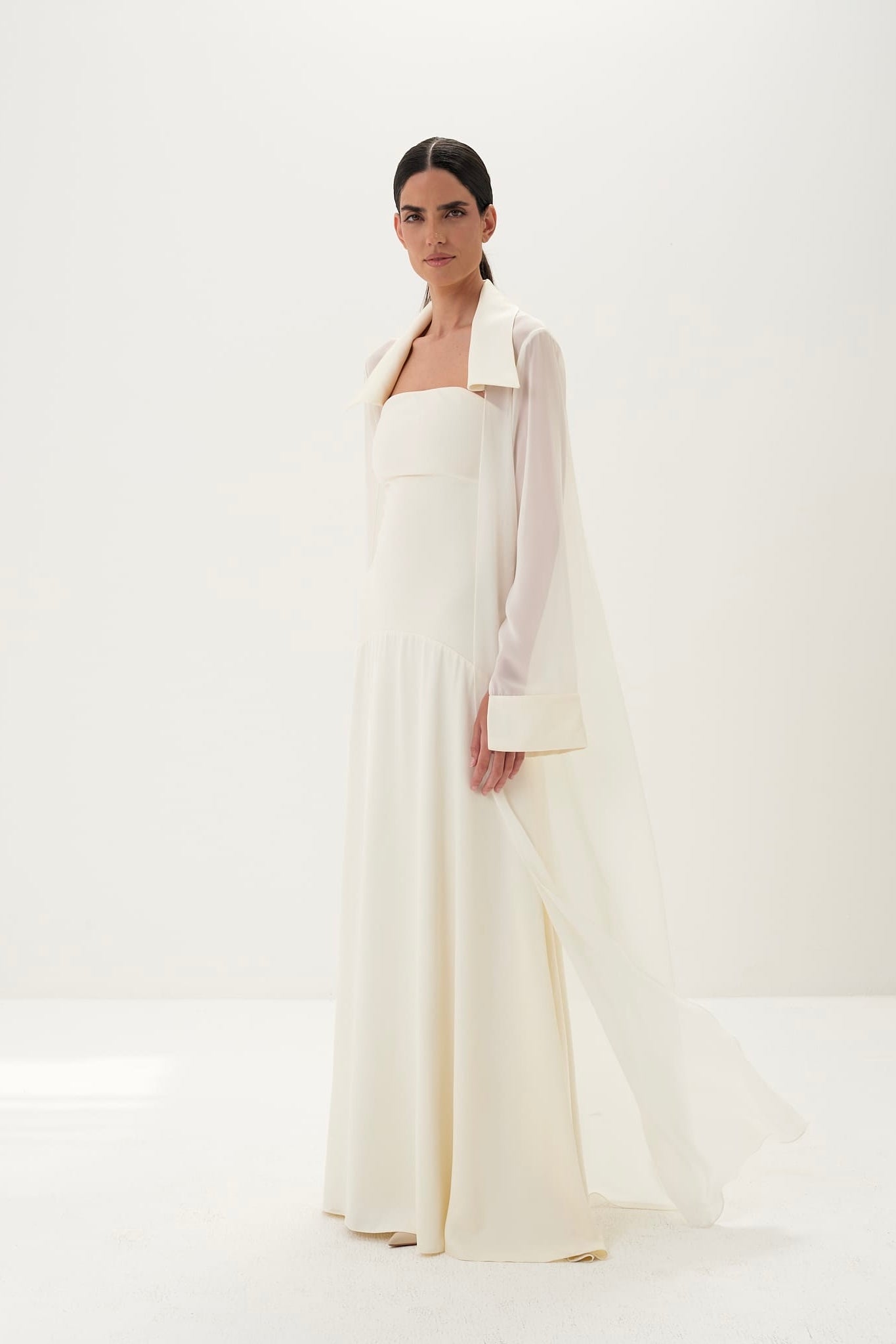 Woman wearing a long white dress with a high collar against a white background