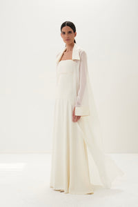Woman wearing a long white dress with a high collar against a white background