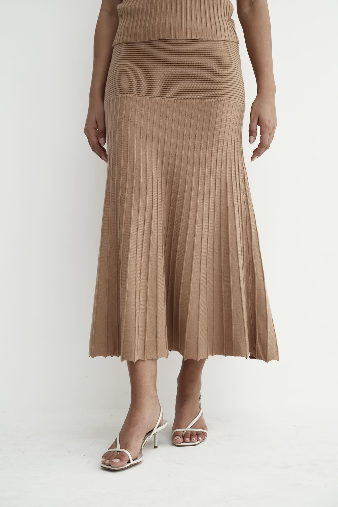 Model wearing Andrea Set, featuring a ribbed sleeveless top and a matching pleated midi skirt, styled with white strappy sandals, posing against a white background