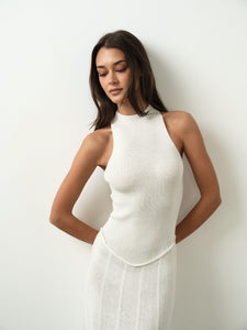 A person with long, dark hair is modeling the sleeveless Asteri Dress in white. They are posing against a plain white backdrop with their hands held behind their back.