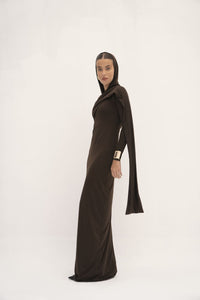 This dress has a sleek, fitted design in a dark, earthy tone with long sleeves and an attached drape that can be wrapped around the head, creating a sophisticated and modest look. The fabric appears smooth, with a slightly matte finish, and the overall silhouette is elongated and elegant. 
