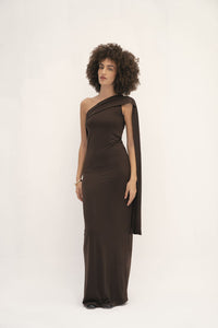 This dress has a sleek, fitted design in a dark, earthy tone with long sleeves and an attached drape that can be wrapped around the head, creating a sophisticated and modest look. The fabric appears smooth, with a slightly matte finish, and the overall silhouette is elongated and elegant. 
