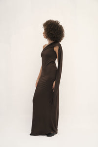 This dress has a sleek, fitted design in a dark, earthy tone with long sleeves and an attached drape that can be wrapped around the head, creating a sophisticated and modest look. The fabric appears smooth, with a slightly matte finish, and the overall silhouette is elongated and elegant. 
