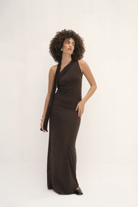 This dress has a sleek, fitted design in a dark, earthy tone with long sleeves and an attached drape that can be wrapped around the head, creating a sophisticated and modest look. The fabric appears smooth, with a slightly matte finish, and the overall silhouette is elongated and elegant. 
