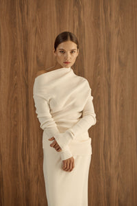 Avani Set in a creamy off-white ribbed knit fabric. The outfit features a long-sleeve asymmetrical draped top paired with a sleek matching skirt, minimalist, elegant aesthetic.