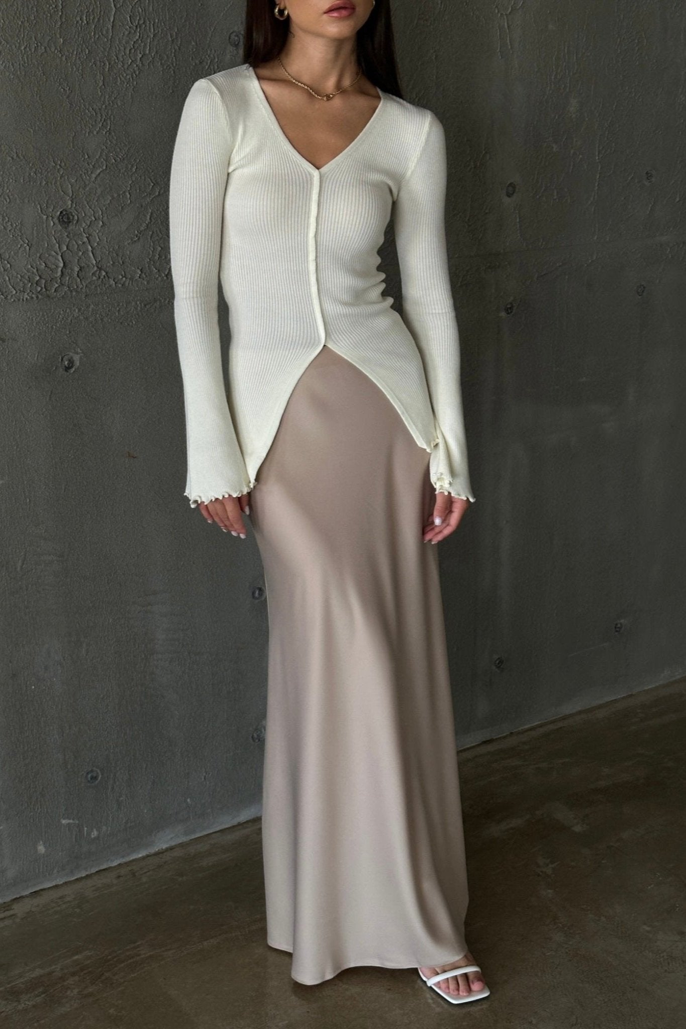 A woman models the Elara knit top, dressed in a white sweater and skirt, exuding sophistication and grace.