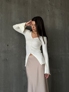 A woman models the Elara knit top, dressed in a white sweater and skirt, exuding sophistication and grace.