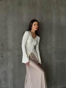 A woman models the Elara knit top, dressed in a white sweater and skirt, exuding sophistication and grace.