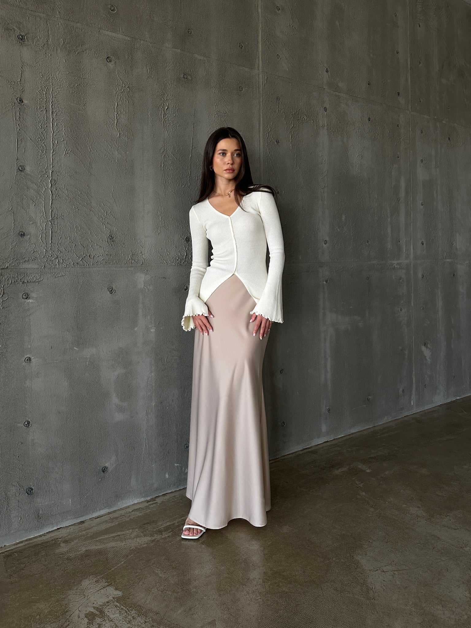 A woman models the Elara knit top, dressed in a white sweater and skirt, exuding sophistication and grace.