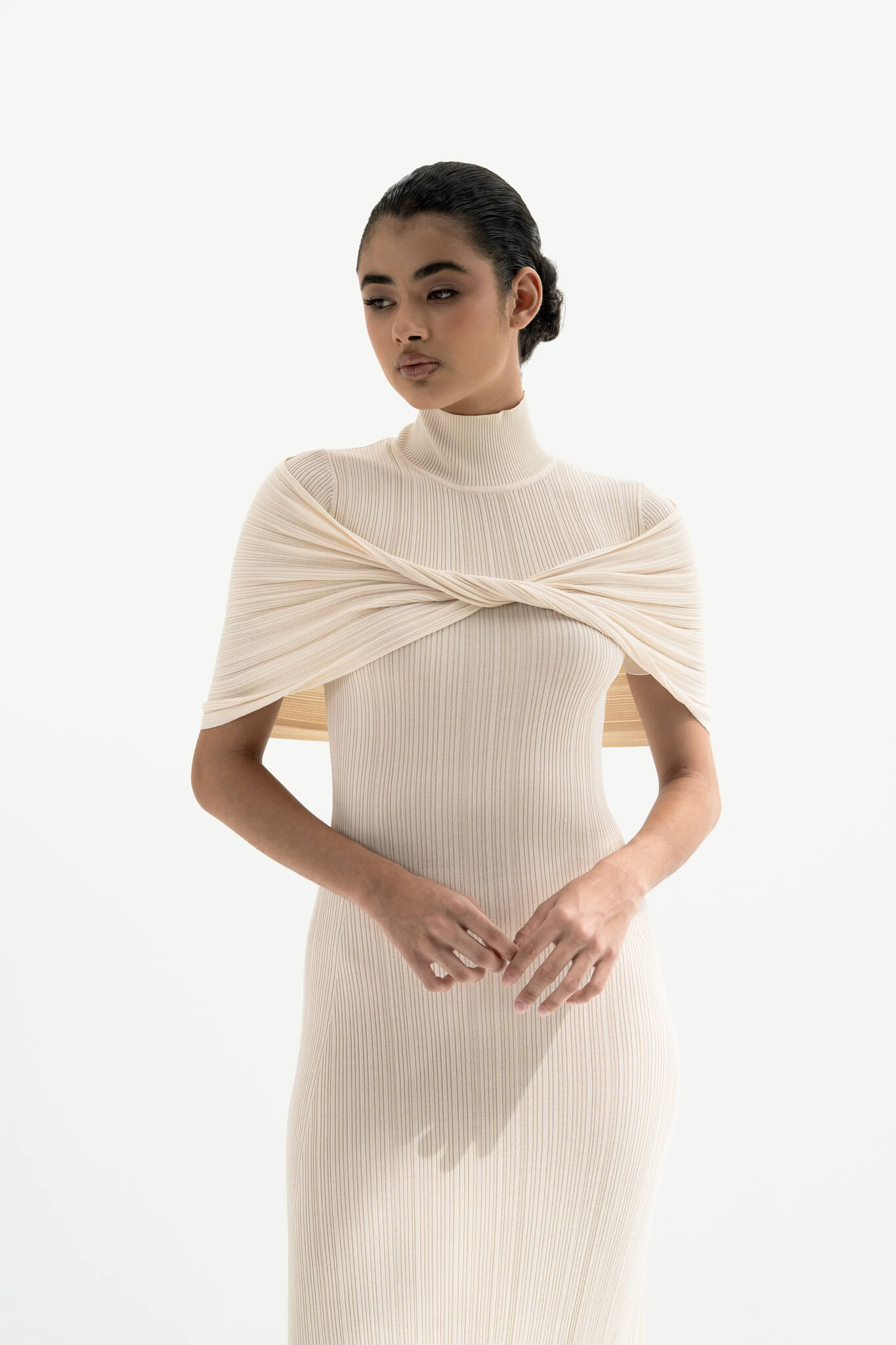 Woman wearing a white ribbed dress with a draped effect on a white background