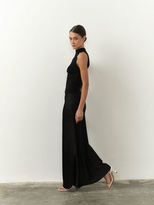 Sleek sleeveless black top featuring a high neck, fitted silhouette, and lightweight fabric, paired with a black satin skirt for a chic and minimalist aesthetic.