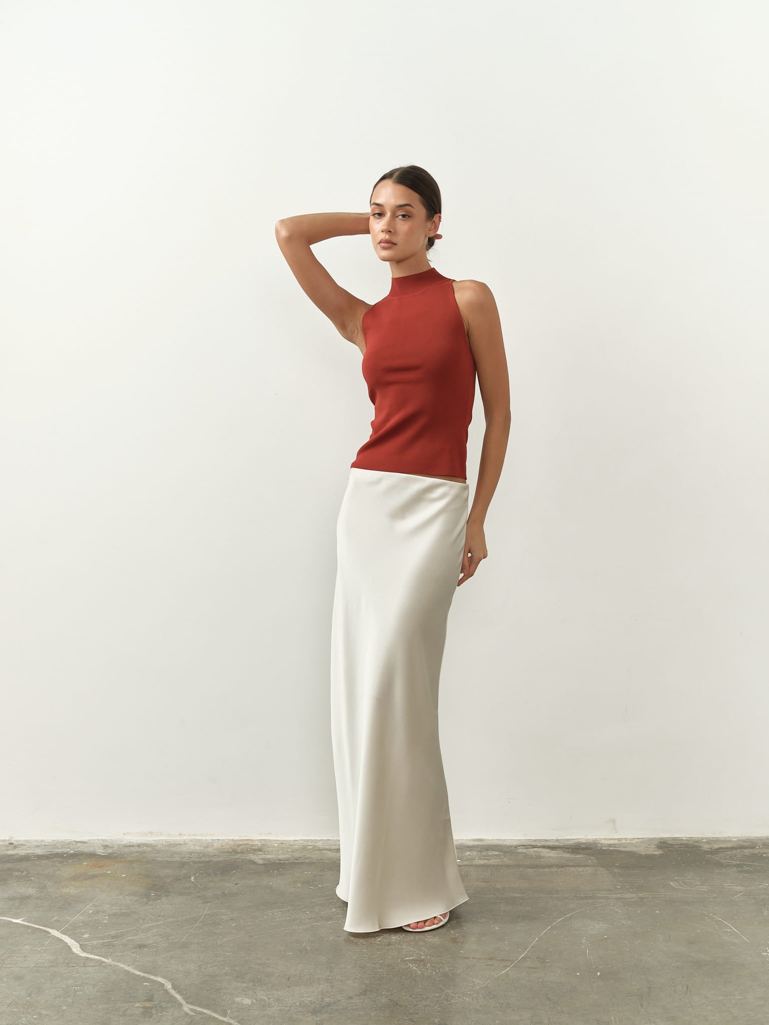 Sleek sleeveless burnt orange top featuring a high neck, fitted silhouette, and lightweight fabric, paired with a satin skirt for a chic and minimalist aesthetic.