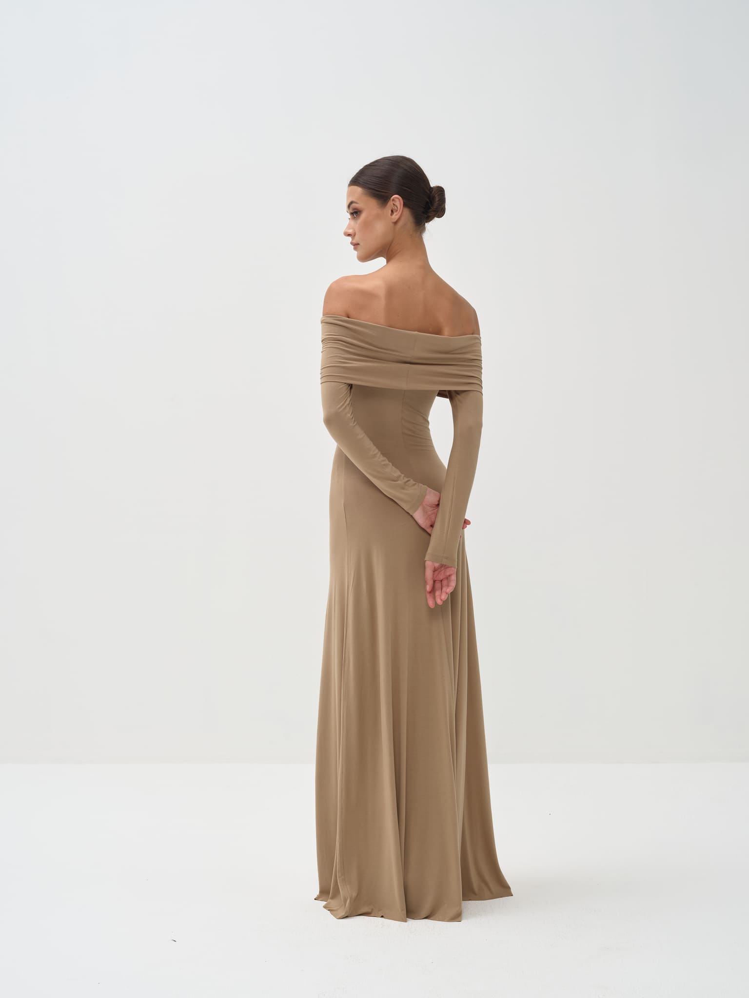 Woman wearing a long, off-shoulder beige dress on a white background