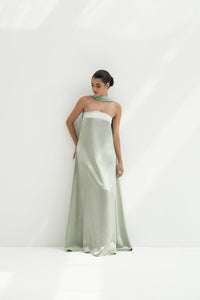 Woman wearing a strapless light green gown with a long scarf on a white background