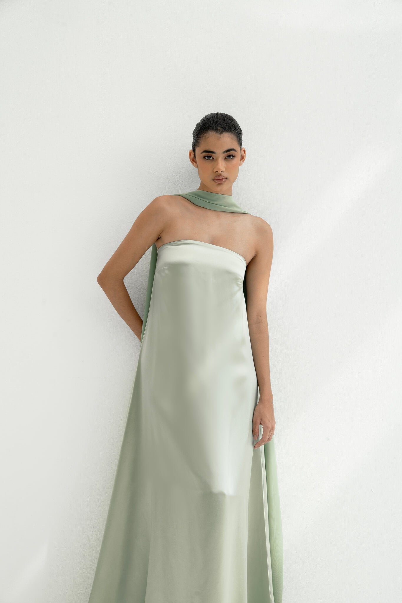 Woman wearing a strapless light green gown with a long scarf on a white background