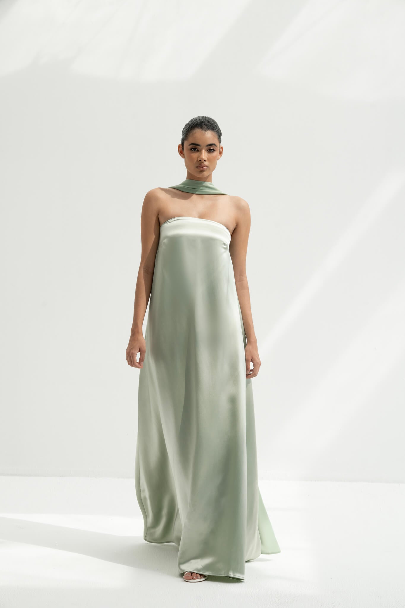 Woman wearing a strapless light green gown with a long scarf on a white background
