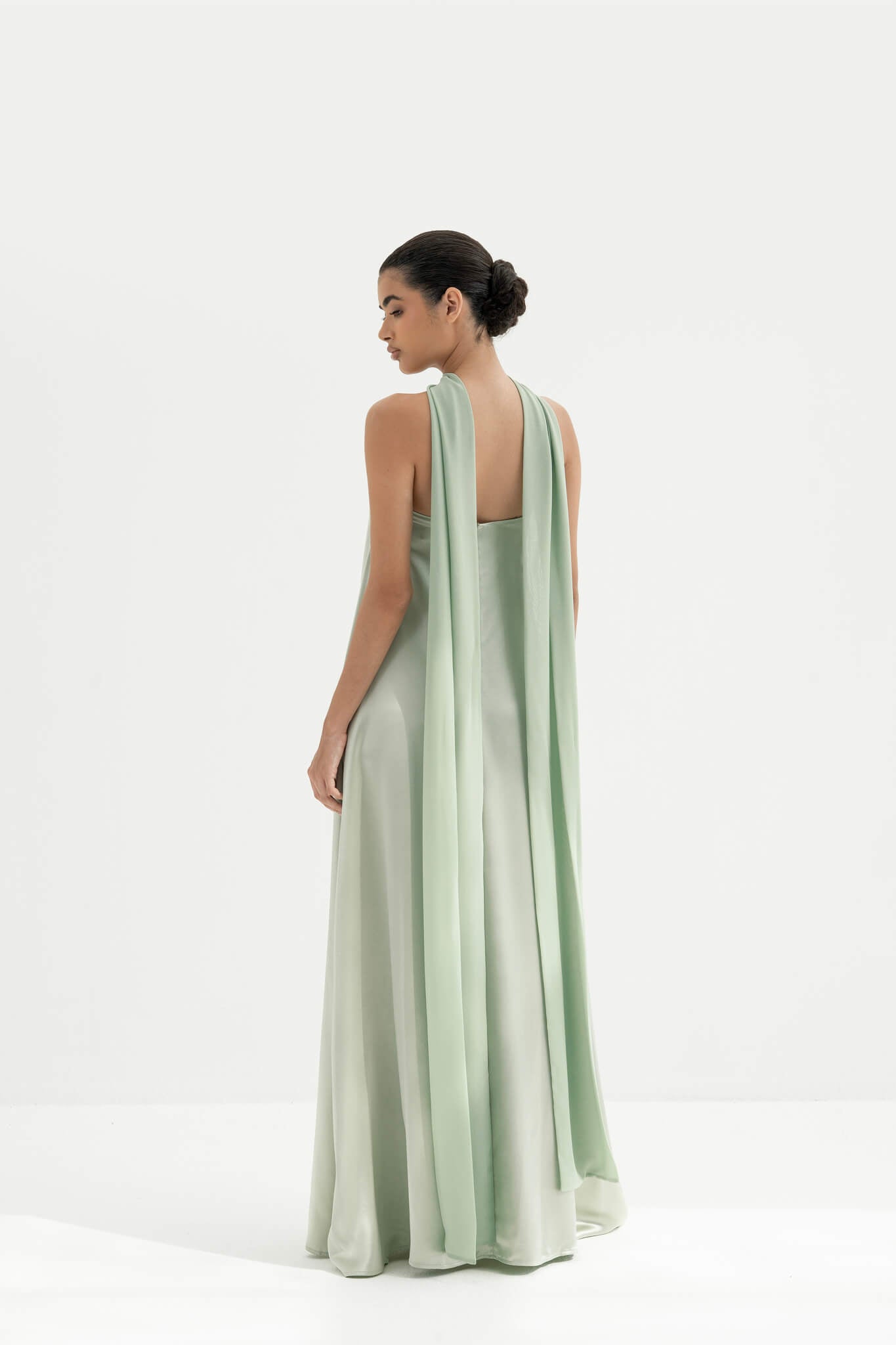 Woman wearing a strapless light green gown with a long scarf on a white background