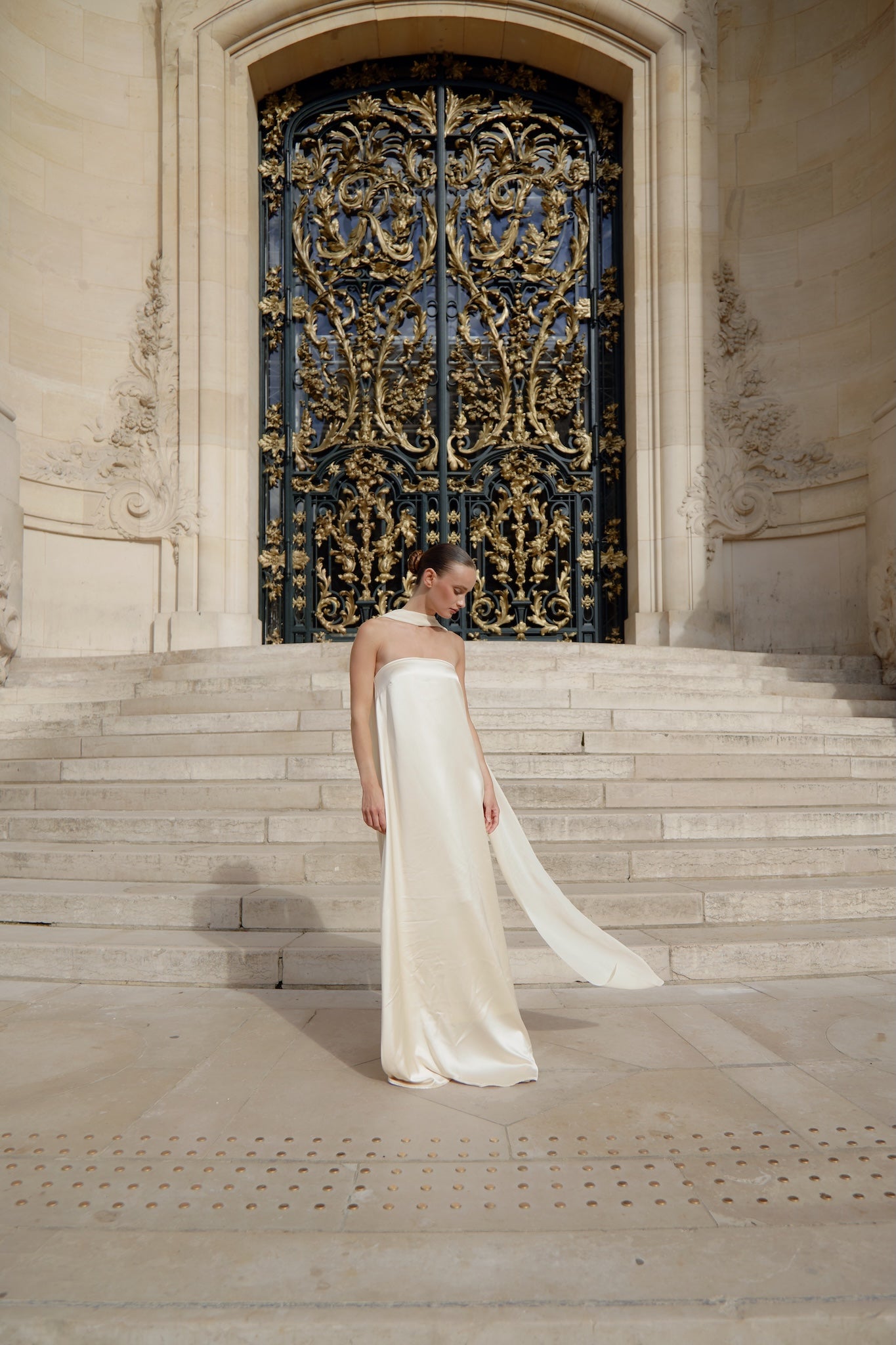 Woman in a white dress standing on steps in front of an ornate black door.