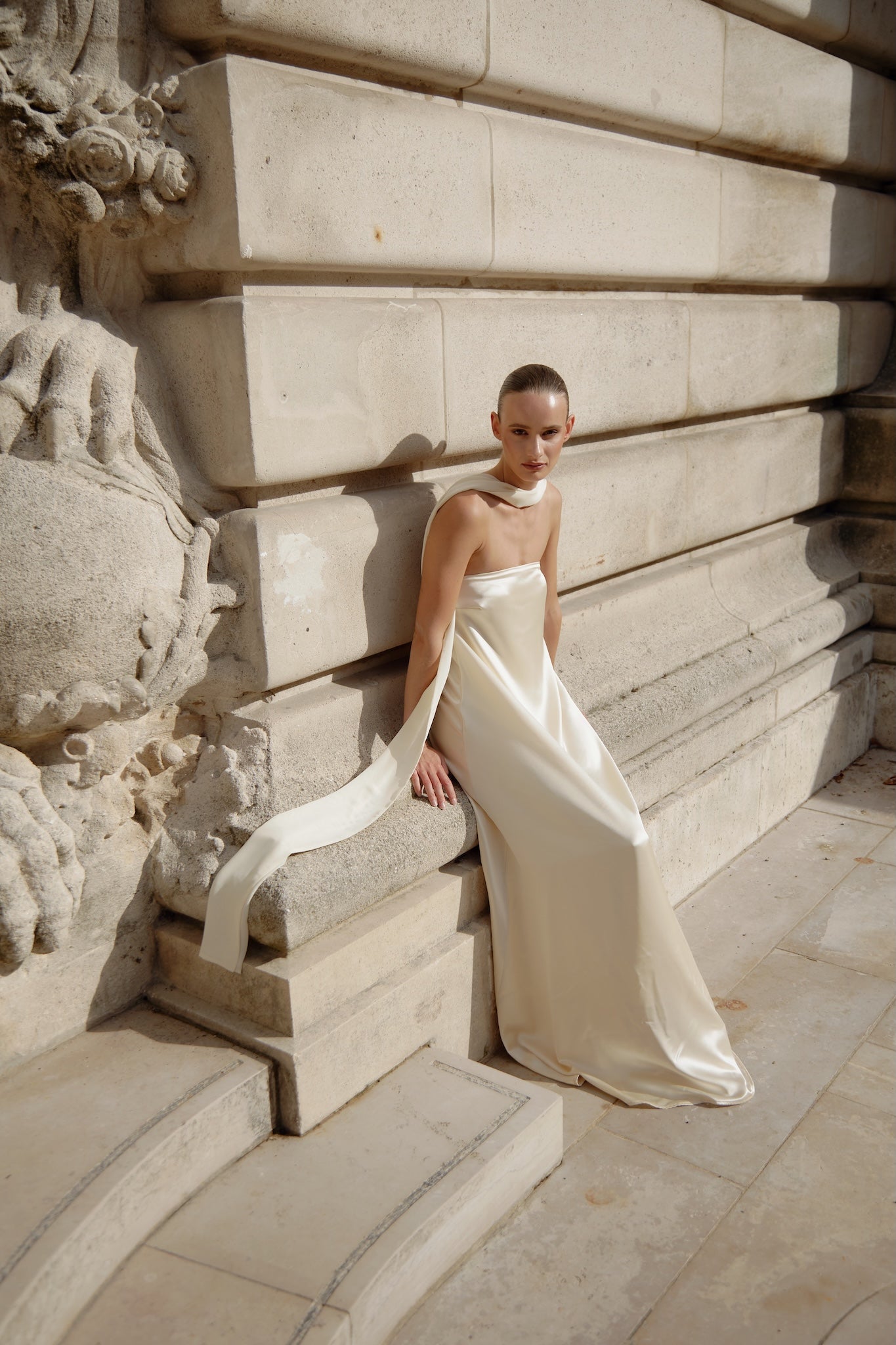 Woman in a white dress sitting on stone steps with classical architecture in the background