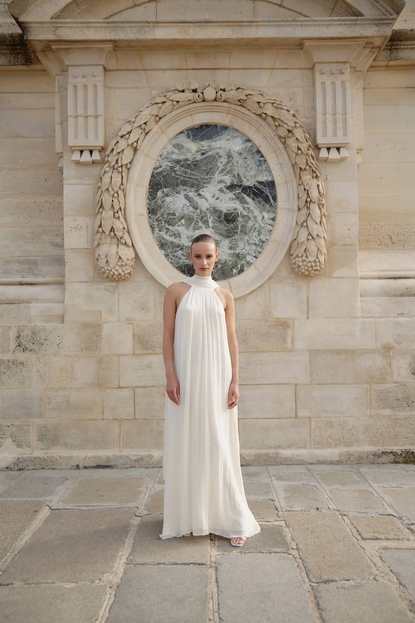 Woman in a white dress standing in front of a decorative stone wall.