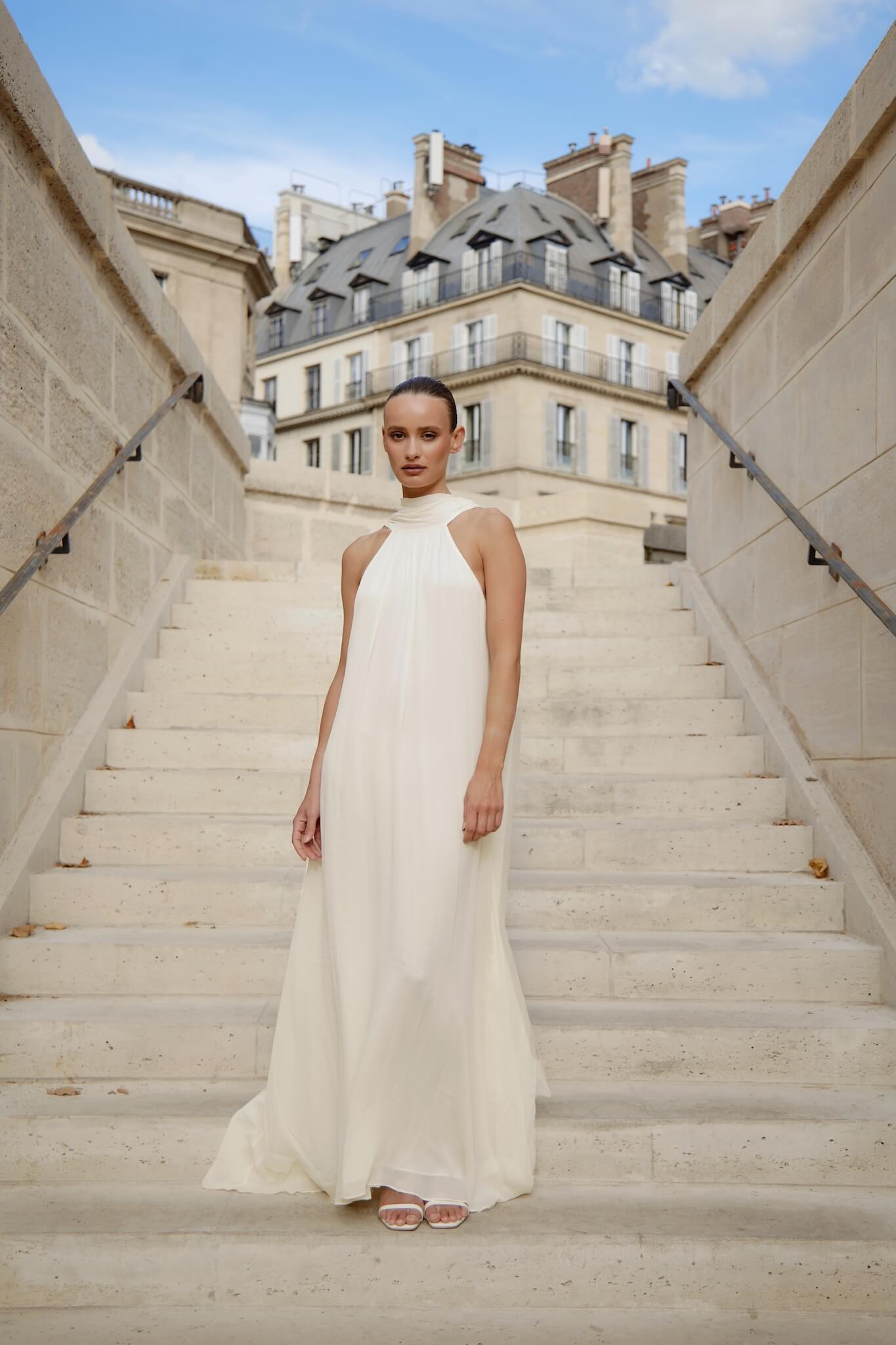 Woman in a white dress standing on stone steps with buildings in the background