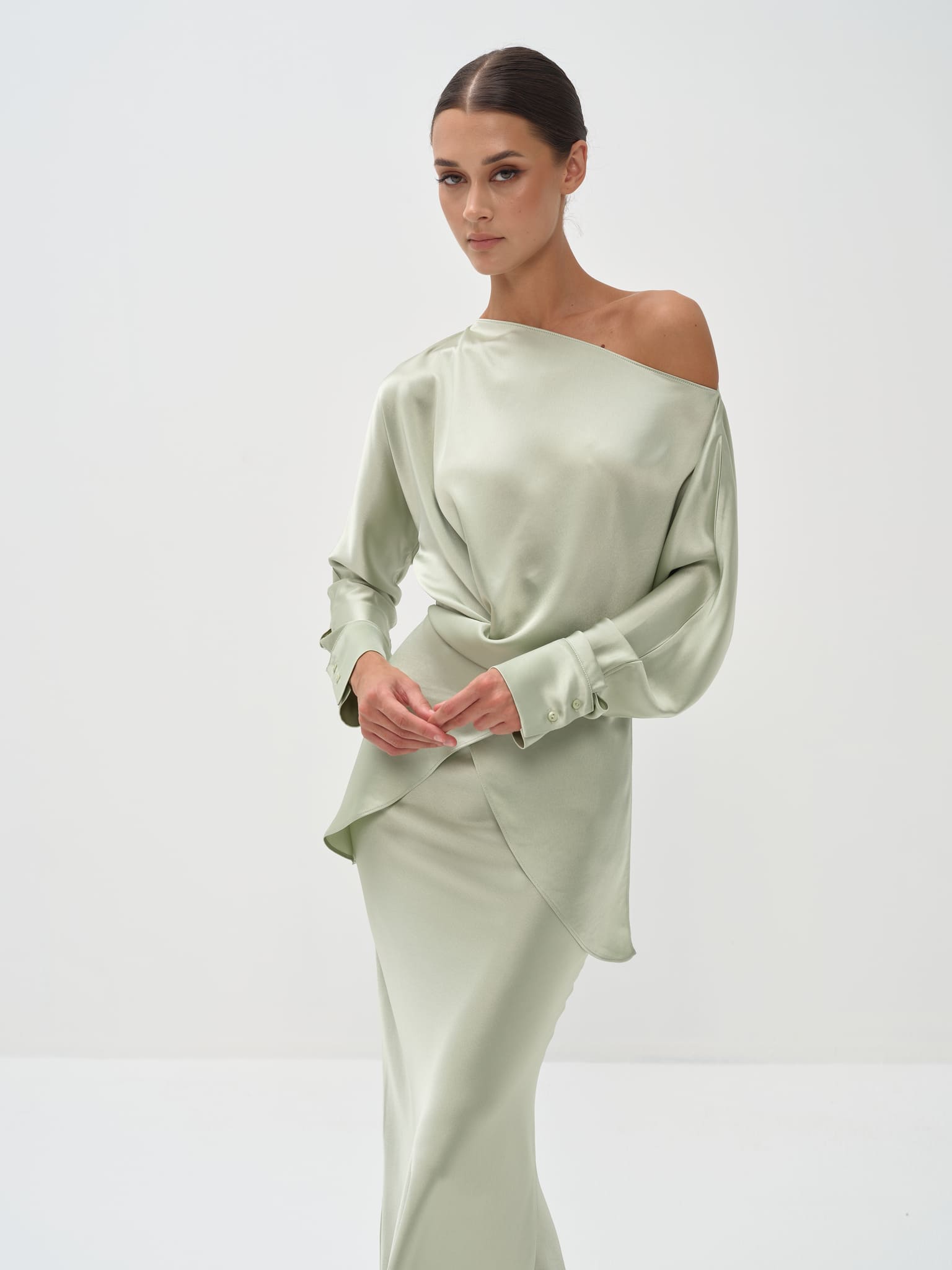 A woman standing against a white background wearing a light green outfit with balloon sleeves and a flowing skirt.