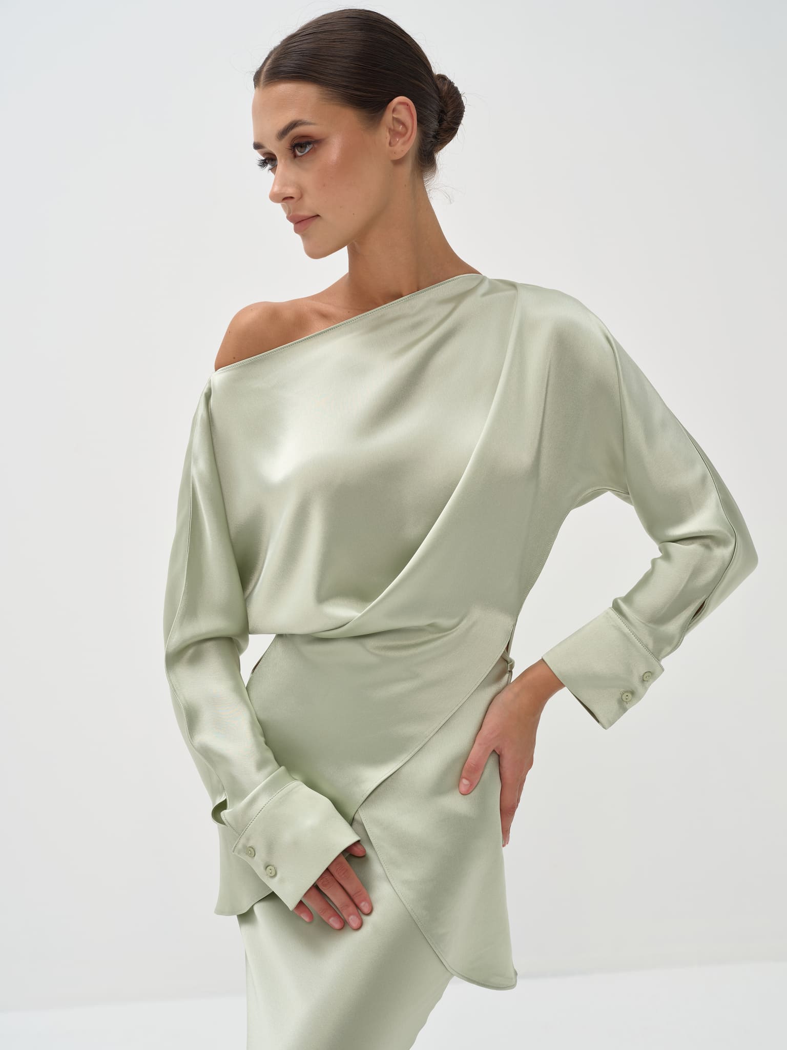 A woman standing against a white background wearing a light green outfit with balloon sleeves and a flowing skirt.
